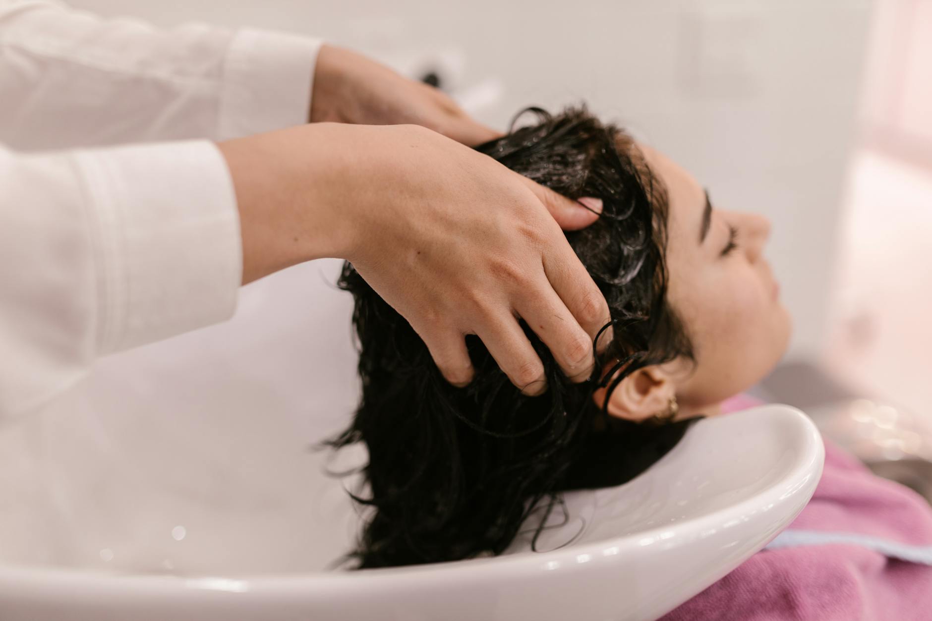 Professional stylist performing scalp massage treatment on client in upscale salon