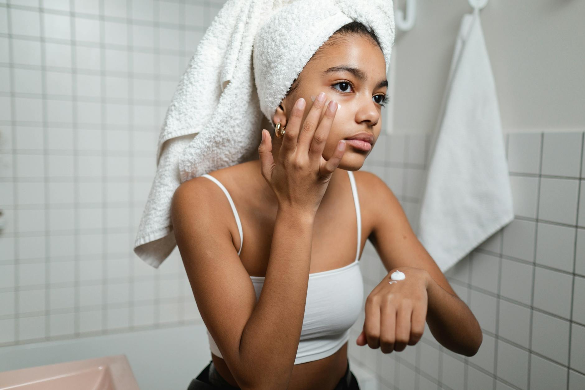 Pregnant woman gently applying facial serum to her cheek during skincare routine