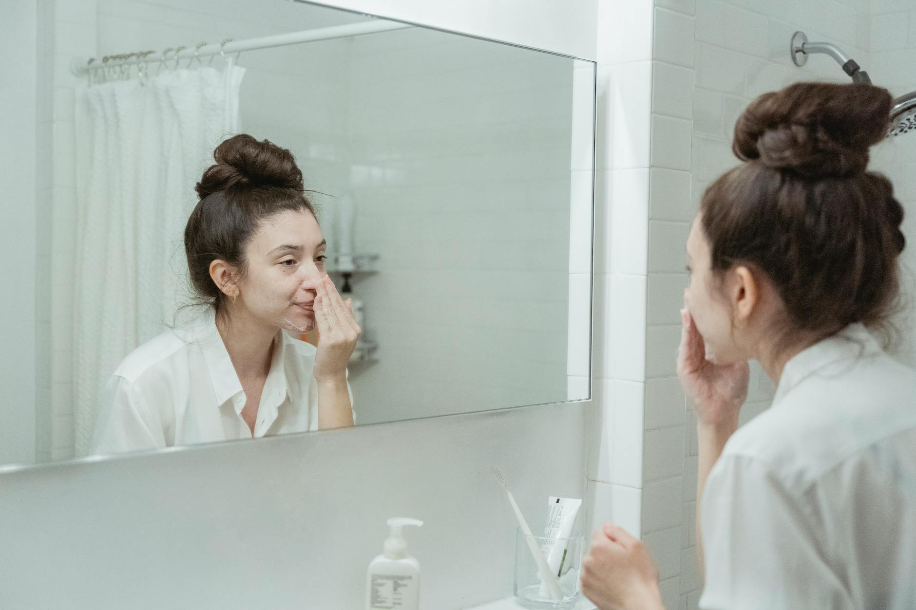 Person looking in mirror during skincare routine with natural lighting and clean aesthetic