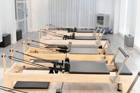 Pilates Reformer Wear Is Quietly Taking Over Brunch Dressing Woman in fitted neutral activewear standing near a pilates reformer machine in a bright studio