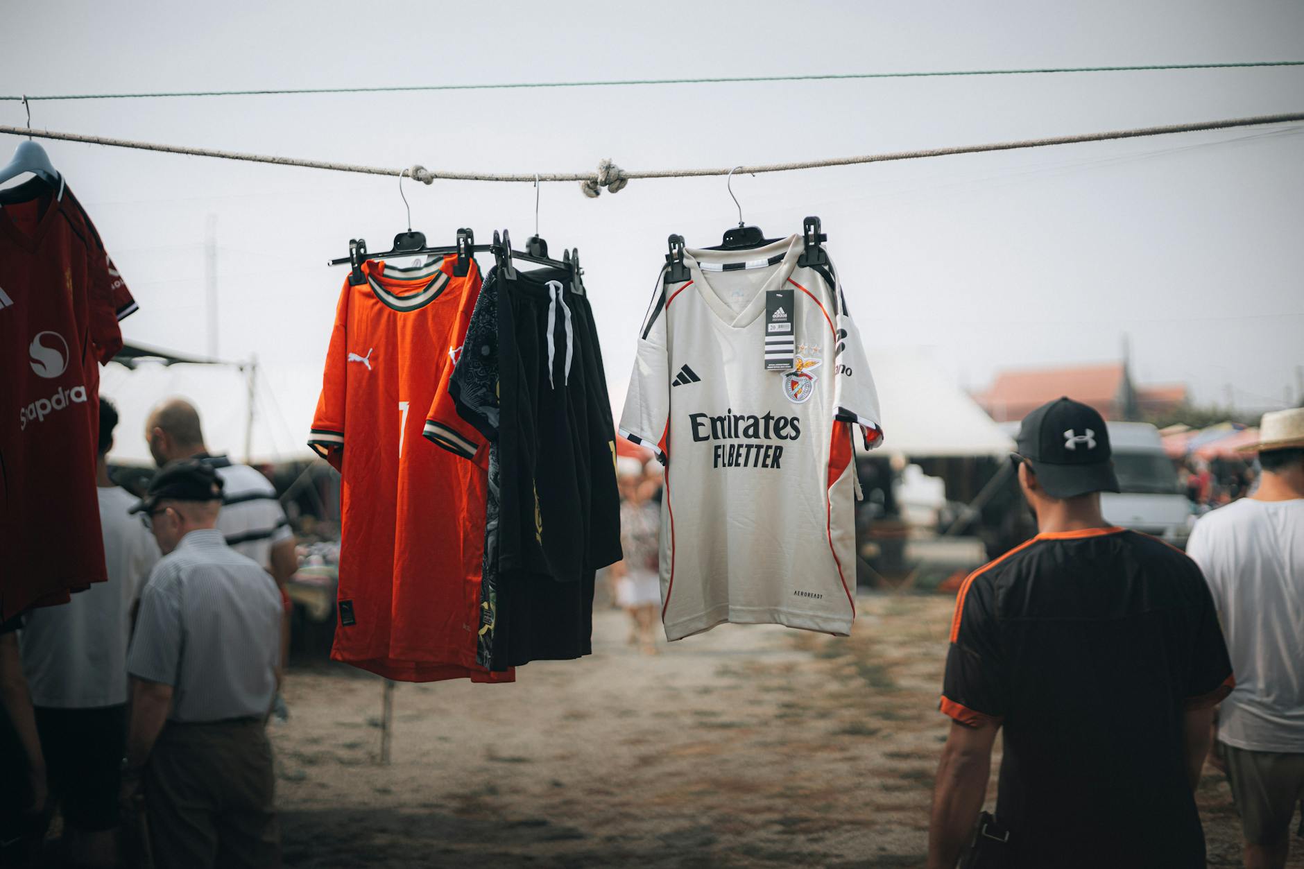 Rack of vintage sportswear pieces at an outdoor market, including faded athletic jerseys and retro sports clothing
