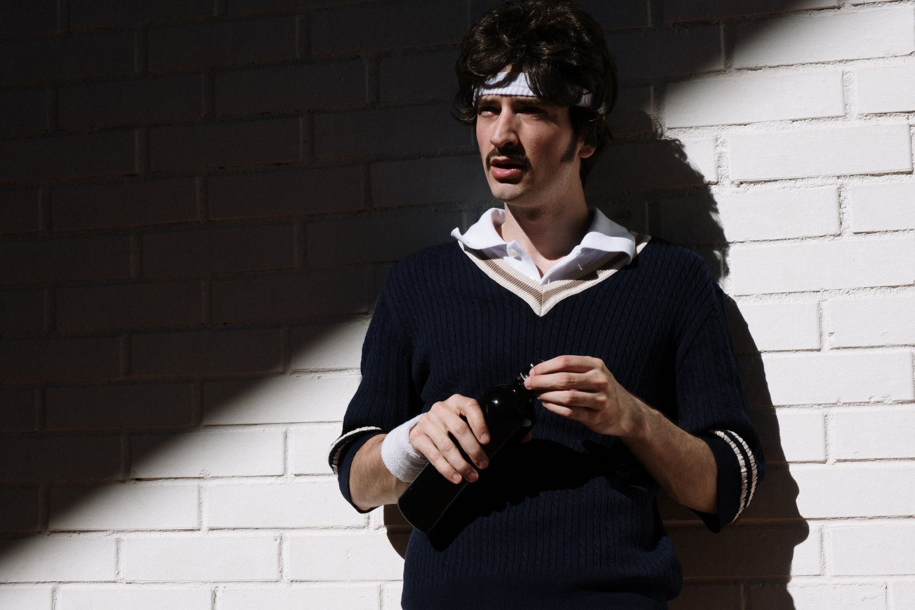 A man wearing a cream cable-knit V-neck sweater layered over a collared shirt with tailored trousers