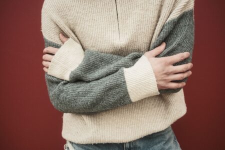 Colorful striped knit pullover folded on a light surface, showing bold horizontal stripe patterns in navy, cream, and gold