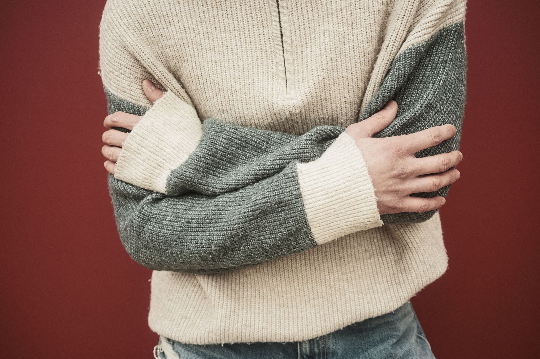 Colorful striped knit pullover folded on a light surface, showing bold horizontal stripe patterns in navy, cream, and gold