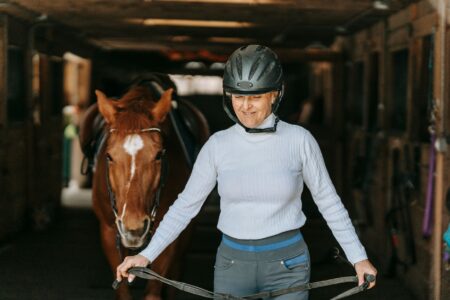 Interior of a horse stable with grooming equipment and protective workwear hanging on wooden stalls