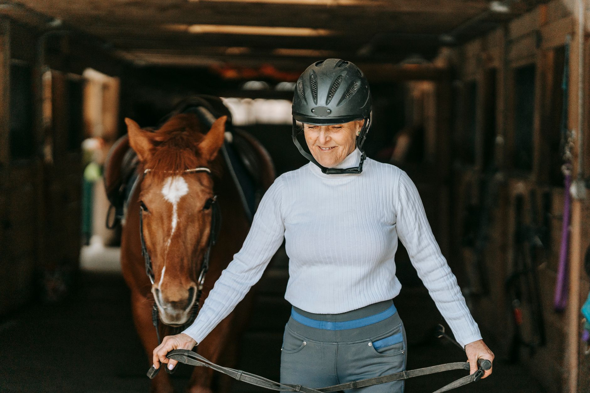 Interior of a horse stable with grooming equipment and protective workwear hanging on wooden stalls
