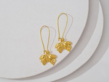 Close-up of elongated gold drop earrings with sculptural abstract form against neutral background