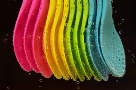 Colourful rowing oar blades lined up by a riverbank, showing bold horizontal stripe patterns in navy, blue, and white